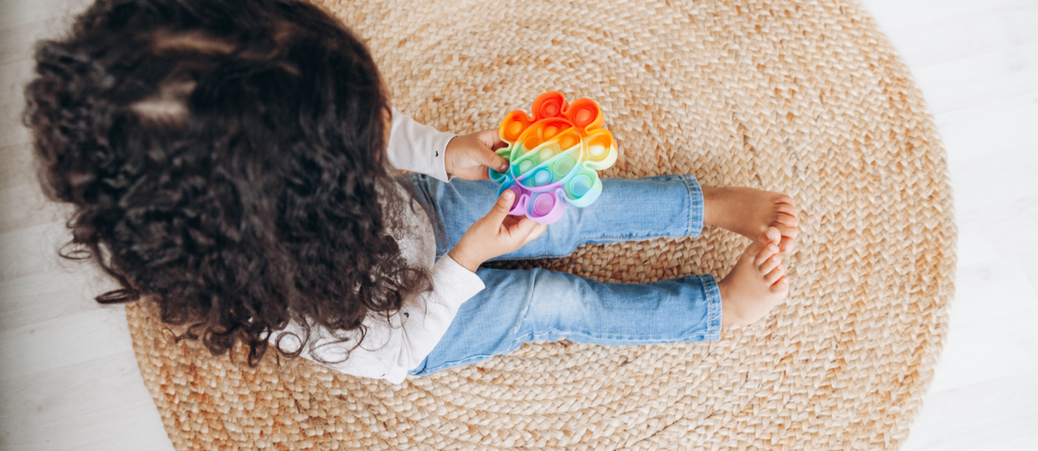 Photo of young child with long curly dark hair playing with a pop fidget toy